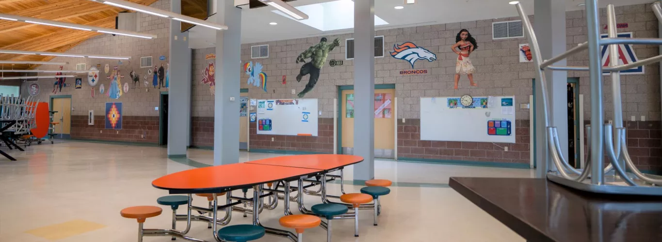 Wingate Elementary School Cafeteria Featuring Modern Architecture, Orange Tables and Stools, Clean Floors, and Juvenile-Themed Wall Hangings and Pictures.