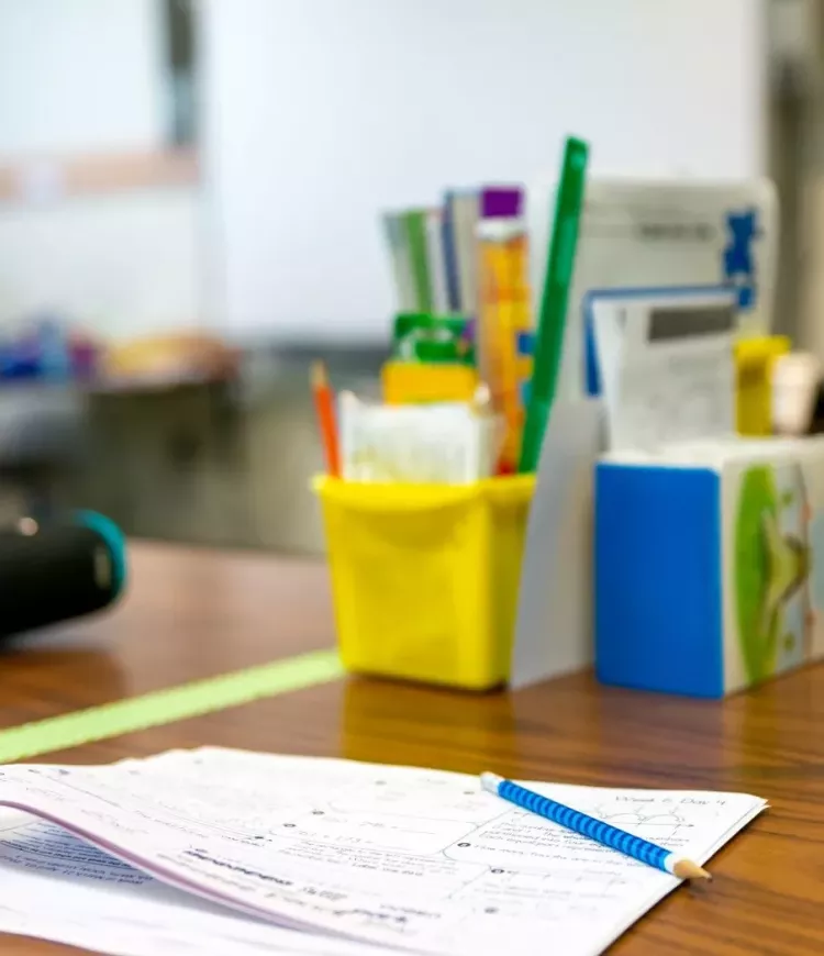 Wingate Elementary School Blurred School Supplies on a Desk with Classwork Papers and a Pencil on Top in Focus.