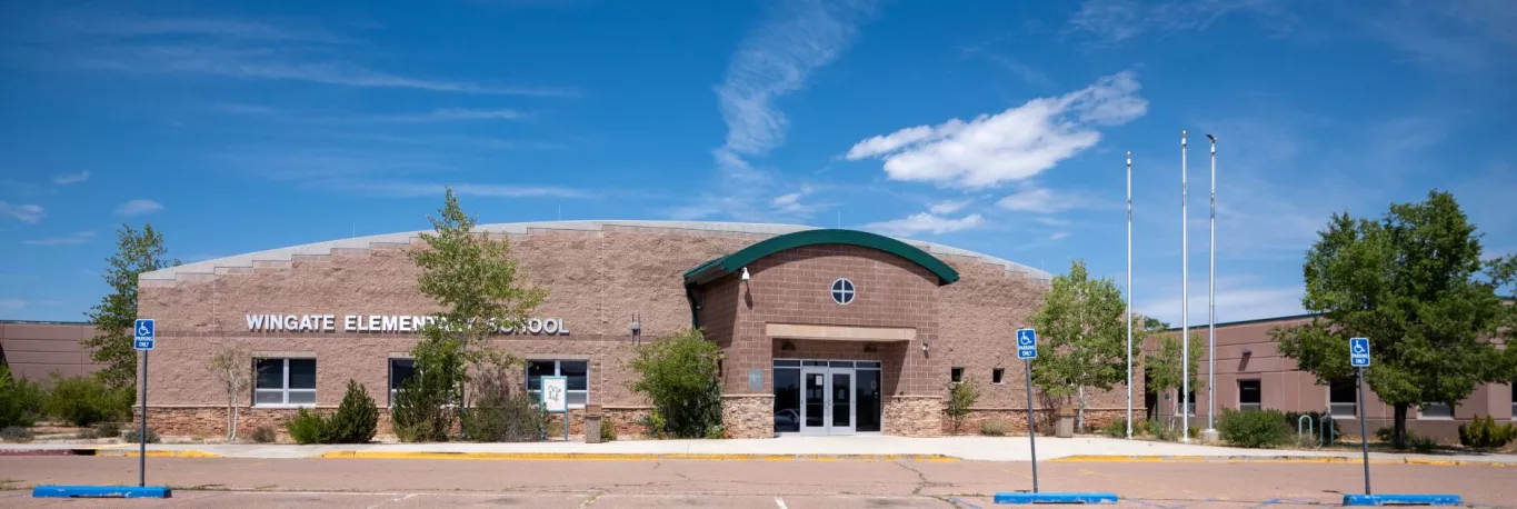 Front View of the Wingate Elementary School including Entrance Doors, Flag Poles, Parking Lot and Beautiful Clear Blue Skies in the Background