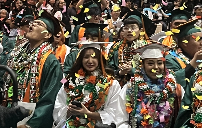 Graduates sitting on chairs while confetti falls from the roof.