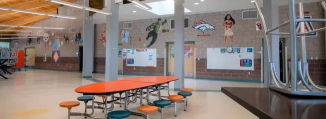 Wingate Elementary School Cafeteria Featuring Modern Architecture, Orange Tables and Stools, Clean Floors, and Juvenile-Themed Wall Hangings and Pictures.